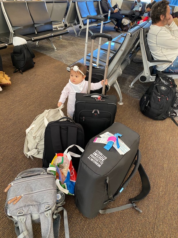 Baby standing in the airport holding onto many pieces of luggage