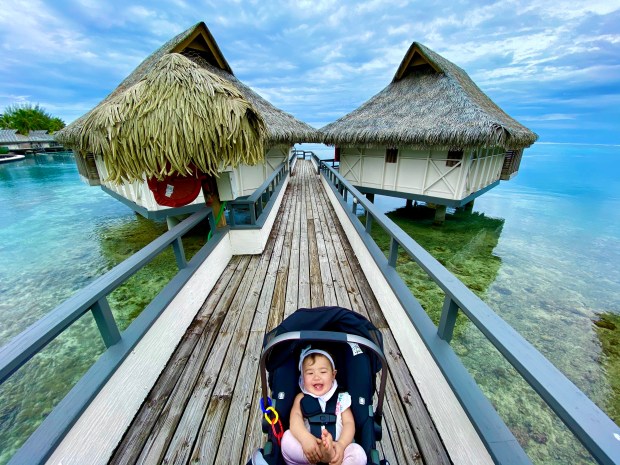Baby laughing near an overwater bungalows in Moorea, French Polynesia